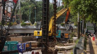 Pekerja dibantu alat berat menyelesaikan pembangunan turap anak Kali Ciliwung di kawasan Pasar Baru, Jakarta, Minggu (29/5/2022). [Suara.com/Angga Budhiyanto]