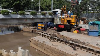 Pekerja dibantu alat berat menyelesaikan pembangunan turap anak Kali Ciliwung di kawasan Pasar Baru, Jakarta, Minggu (29/5/2022). [Suara.com/Angga Budhiyanto]