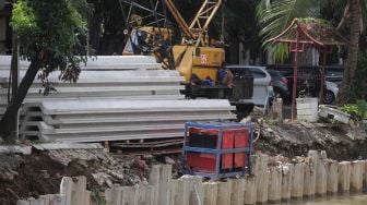 Pekerja beristirahat di sela menyelesaikan pembangunan turap anak Kali Ciliwung di kawasan Pasar Baru, Jakarta, Minggu (29/5/2022). [Suara.com/Angga Budhiyanto]