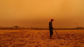 Seorang remaja menggunakan metal detector saat badai pasir melanda di atas kota Zardana, provinsi Idlib, Suriah, Kamis (2/6/2022). [Abdulaziz KETAZ / AFP]
