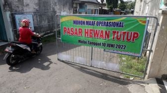 Warga melewati pintu gerbang pasar hewan Muning yang ditutup sementara di Kota Kediri, Jawa Timur, Jumat (10/6/2022).ANTARA FOTO/Prasetia Fauzani