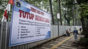 Warga berjalan di dekat spanduk informasi penutupan sementara Tebet Eco Park di Tebet, Jakarta, Rabu (15/6/2022). ANTARA FOTO/Aprillio Akbar