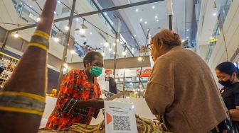 Seorang pembeli (kanan) melakukan transaksi digital di stan Sanggar Noken Aniya saat pameran produksi lokal di Mal Jayapura, Papua, Jumat (24/6/2022). [ANTARA FOTO/Indrayadi TH/foc]