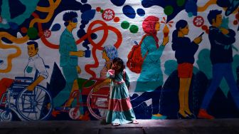 Anak-anak bermain dengan latar belakang mural bertema Jakarta Kota Global di Terowongan Kendal, Jakarta Pusat, Senin (27/6/2022). [Suara.com/Alfian Winanto]