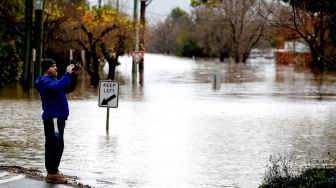 Seorang warga memotret jalanan yang banjir akibat hujan deras di pinggiran Camden, Sydney, Australia, Minggu (3/7/2022). [Muhammad FAROOQ / AFP]
