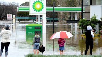 Warga berdiri di samping SPBU yang banjir akibat hujan deras di pinggiran Camden, Sydney, Australia, Minggu (3/7/2022). [Muhammad FAROOQ / AFP]

