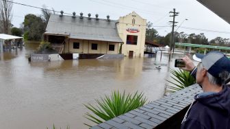 Seorang warga merekam jalanan yang banjir akibat hujan deras di pinggiran Camden, Sydney, Australia, Minggu (3/7/2022). [Muhammad FAROOQ / AFP]
