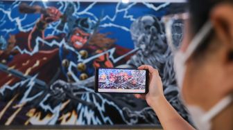 Warga melihat mural kolaborasi bergambar Thor dengan smartphonenya di Terowongan Kendal, Jakarta Pusat, Selasa (5/7/2022). [Suara.com/Alfian Winanto]