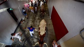 Peserta dan banteng berlari keluar dari kandang selama acara "encierro" (lari banteng)saat festival San Fermin di Pamplona, Spanyol, Kamis (7/7/2022). [JOSE JORDAN / AFP]