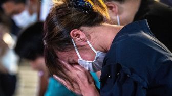 Seorang warga menangis saat berdoa untuk mantan Perdana Menteri Jepang Abe Shinzo di TKP penembakan di luar Stasiun Yamato Saidaiji di Nara, Jepang, Jumat (8/7/2022). [Philip FONG / AFP]