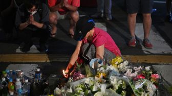 Warga menaruh bunga dan berdoa untuk mantan Perdana Menteri Jepang Abe Shinzo di TKP penembakan di luar Stasiun Yamato Saidaiji di Nara, Jepang, Jumat (8/7/2022). [Philip FONG / AFP]
