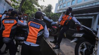 Petugas mengangkut sepeda motor yang parkir liar ke atas truk di lokasi Citayam Fashion Week di kawasan Dukuh Atas, Jakarta Pusat, Selasa (26/7/2022). [Suara.com/Alfian Winanto]