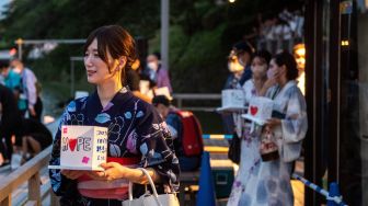 Seorang wanita memakai Yukata memegang lentera kertas sebelum naik perahu saat festival lentera terapung di Chidorigafuchi, Tokyo, Jepang, Jumat (29/7/2022). [Philip FONG / AFP]