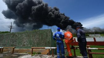 Pekerja Cuban Petroleum (CUPET) melihat asap hitam akibat kebakaran di tangki minyak di Matanzas, Kuba, Sabtu (6/8/2022). [Yamil LAGE / AFP]