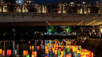 Warga melihat lentera kertas di Sungai Motoyasu untuk memperingati 77 tahun serangan bom atom di samping kubah bom atom, Hiroshima, Jepang, Sabtu (6/8/2022). [Philip FONG / AFP]
