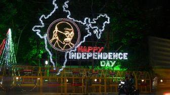Seorang pengendara melewati instalasi lampu yang menunjukkan gambar ikon kemerdekaan India,  Mahatma Gandhi dan peta India di Chennai, India, Sabtu (13/8/2022). [Arun SANKAR / AFP]