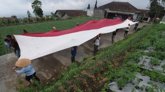 Petani lereng Gunung Merbabu mengirabkan kain Merah Putih yang akan dibentangkan di lahan pertanian lereng Gunung Merbabu, Selo, Boyolali, Jawa Tengah, Selasa (16/5/2022).