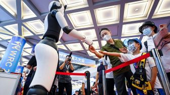 Pengunjung berjabat tangan dengan sebuah Robot pada acara Konferensi Robot Dunia 2022 di Beijing, China, Kamis (18/8/2022). [WANG Zhao/AFP]
