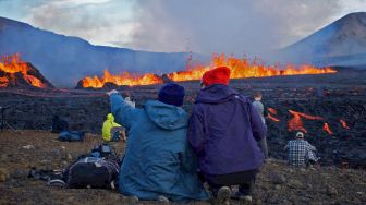 Sejumlah orang melihat semburan dan aliran lava dari  di Grindavik, Islandia, Rabu (3/8/2022). [Jeremie RICHARD / AFP]