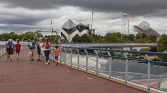 Pengunjung berjalan di sebuah jembatan di taman hiburan Futuroscope ddi Chasseneuil-du-Poitou, Prancis, Jumat (19/8/2022). [GUILLAUME SOUVANT / AFP]
