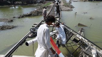 Warga terdampak banjir melintasi rel kereta api yang rusak diterjang banjir di kawasan Fazilpur, Provinsi Punjab, Pakistan, Sabtu (3/9/2022). [Arif ALI / AFP]
