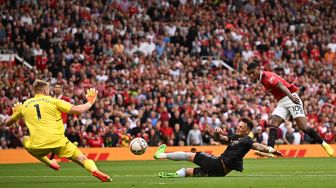 Striker Manchester United Marcus Rashford (kanan) menendang bola melewati bek Arsenal Ben White dan kiper Arsenal Aarron Ramsdale (kiri) untuk mencetak gol saat pertandingan sepak bola Liga Premier Inggris antara Manchester United dan Arsenal di Stadion Old Trafford, Manchester, Inggris, Minggu (4/9/2022). [Oli SCARFF / AFP]