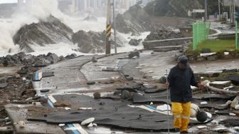 Seorang pria berjalan di sepanjang jalan yang rusak akibat Topan Hinnamnor di Ulsan, Korea Selatan, Selasa (6/9/2022). [YONHAP/AFP]
