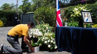 Seorang pengunjung meletakkan bunga belasungkawa di sebelah buku dan potret mendiang Ratu Elizabeth II di British Residence, Mexico City, Meksiko, Jumat (9/9/2022). [CLAUDIO CRUZ / AFP]