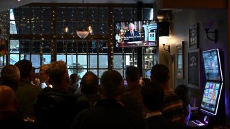 Para pengunjung di sebuah pub menonton pidato Raja Inggris Charles III yang disiarkan televisi secara langsung dari Istana Buckingham di London, Inggris, Jumat (9/9/2022). [JUSTIN TALLIS / AFP]