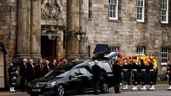 Petugas membawa peti jenazah mendiang Ratu Elizabeth II Inggris yang ditutupi dengan bendera Royal Standard of Scotland saat tiba di Istana Holyroodhouse, Edinburgh, Skotlandia, Minggu (11/9/2022). [ALKIS KONSTANTINIDIS / POOL / AFP]
