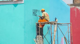 Sejumlah petugas Penanganan Prasarana & Sarana Umum (PPSU) menyelesaikan pembuatan mural di Kampung Gembira Gembrong, Jakarta Timur, Rabu (14/9/2022). [Suara.com/Alfian Winanto]