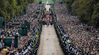 Warga Inggris menyaksikan iring-iringan yang membawa peti mati Ratu elizabeth II saat tiba di Kastil Windsor, Inggris, Senin (19/9/2022). [CARL DE SOUZA / POOL / AFP]
