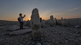 Turis mengunjungi situs megalitik Dolmen of Guadalperal yang muncul kembali setelah air Waduk Valdecanas surut akibat kekeringan yang melanda di Peraleda de la Mata, Spanyol, Kamis (28/8/2022). [PIERRE-PHILIPPE MARCOU / AFP ]
