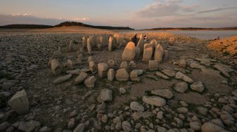 Turis mengunjungi situs megalitik Dolmen of Guadalperal yang muncul kembali setelah air Waduk Valdecanas surut akibat kekeringan yang melanda di Peraleda de la Mata, Spanyol, Kamis (28/8/2022). [PIERRE-PHILIPPE MARCOU / AFP ]
