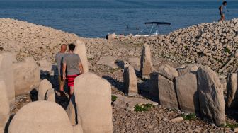 Turis mengunjungi situs megalitik Dolmen of Guadalperal yang muncul kembali setelah air Waduk Valdecanas surut akibat kekeringan yang melanda di Peraleda de la Mata, Spanyol, Kamis (28/8/2022). [PIERRE-PHILIPPE MARCOU / AFP ]
