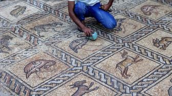 Putra petani Palestina Salman al-Nabahin saat membersihkan mozaik Bizantium yang ditemukan oleh ayahnya ketika menggali tanah di Bureij, Gaza, Palestina, Minggu (18/9/2022). [AFP PHOTO/MOHAMMED ABED]
