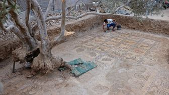 Putra petani Palestina Salman al-Nabahin saat membersihkan mozaik Bizantium yang ditemukan oleh ayahnya ketika menggali tanah di Bureij, Gaza, Palestina, Minggu (18/9/2022). [AFP PHOTO/MOHAMMED ABED]