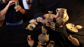 Petugas dari Israel Antiquities Authority (IAA) memegang salah satu bejana yang diyakini berisi opium dari abad ke-14 SM yang ditemukan di situs pemakaman Tel Yehud dan sekarang dipajang di kantor IAA di Yerusalem, Israel, Selasa (20/9/2022). [AHMAD GHARABLI/AFP]