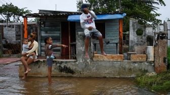 Sebuah keluarga terlihat di luar rumah mereka yang terendam banjir usai diterjang Badai Ian di Batabano, Kuba, Selasa (27/9/2022). [YAMIL LAGE/AFP]