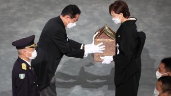 Perdana Menteri Jepang Fumio Kishida (kedua dari kiri) menyerahkan guci abu mantan perdana menteri Jepang Shinzo Abe kepada Istrinya Akie Abe saat pemakaman kenegaraan di Nippon Budokan, Tokyo, Jepang, Selasa (27/9/2022). [Takashi Aoyama / POOL / AFP]