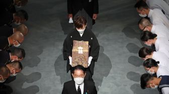 Istri mendiang mantan Perdana Menteri Jepang Shinzo Abe, Akie Abu membawa abu suaminya saat pemakaman kenegaraan di Nippon Budokan, Tokyo, Jepang, Selasa (27/9/2022). [Takashi Aoyama / POOL / AFP]