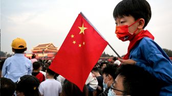 Seorang anak memegang bendera nasional China ketika orang-orang berkumpul di dekat Lapangan Tiananmen untuk upacara pengibaran bendera pada Hari Nasional China di Beijing, Sabtu (1/20/2022). [Noel SELIS / AFP]