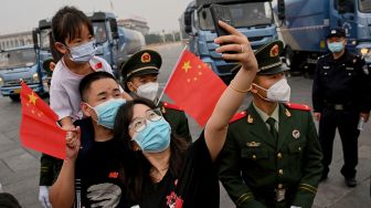 Seorang wanita menggunakan ponsel untuk berfoto selfie di depan tentara di Lapangan Tiananmen setelah upacara pengibaran bendera pada Hari Nasional China di Beijing, Sabtu (1/20/2022). [Noel SELIS / AFP]