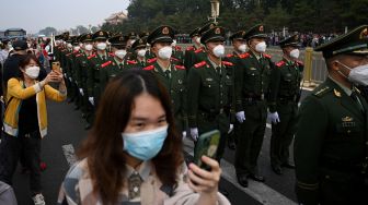 Orang-orang menggunakan ponsel mereka untuk mengambil foto tentara di Lapangan Tiananmen setelah upacara pengibaran bendera pada Hari Nasional China di Beijing, Sabtu (1/20/2022). [Noel SELIS / AFP]