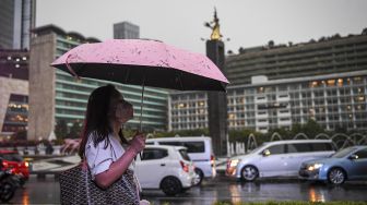 Seorang warga menggunakan payung saat turun di kawasan Bundaran Hotel Indonesia, Jakarta, Selasa (4/10/2022).  ANTARA FOTO/M Risyal Hidayat