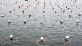 Sejumlah prajurit TNI dan Polri serta sipil mengapung di air tanpa berpindah tempat (Water Trappen) membentuk tulisan 'TNI 77' di Perairan Pantai Marina, Jakarta, Rabu (5/10/2022). [ANTARA FOTO/M Risyal Hidayat/nz]