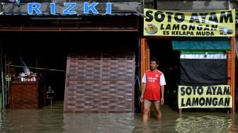 Warga berdiri di depan lokasi usahanya yang terendam banjir di kawasan Pura Demak, Denpasar, Bali, Sabtu (8/10/2022). ANTARA FOTO/Fikri Yusuf
