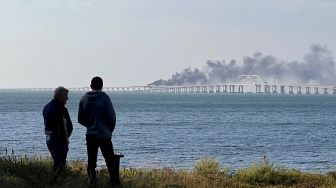 Orang-orang melihat asap hitam mengepul dari kebakaran akibat sebuah truk yang meledak di jembatan Kerch yang menghubungkan Krimea dan Rusia di semenanjung Kerch, Sabtu (8/10/2022). [Roman DMITRIYEV / AFP]