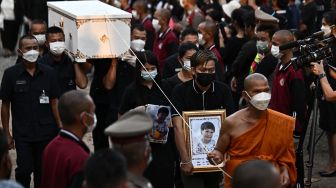 Seorang biksu dan kerabat berjalan dengan peti mati korban penembakan massal selama upacara kremasi di Na Klang, Provinsi Nong Bua Lam Phu, Thailand, Selasa (11/10/2022). [Lillian SUWANRUMPHA / AFP]