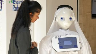 Seorang wanita berdiri di dekat robot selama pameran teknologi GITEX Global di Dubai World Trade Center (DWTC) di Uni Emirat Arab, Rabu (12/10/2022). [Karim SAHIB / AFP]
